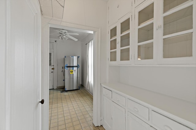 interior space featuring white cabinets, ceiling fan, glass insert cabinets, freestanding refrigerator, and light countertops