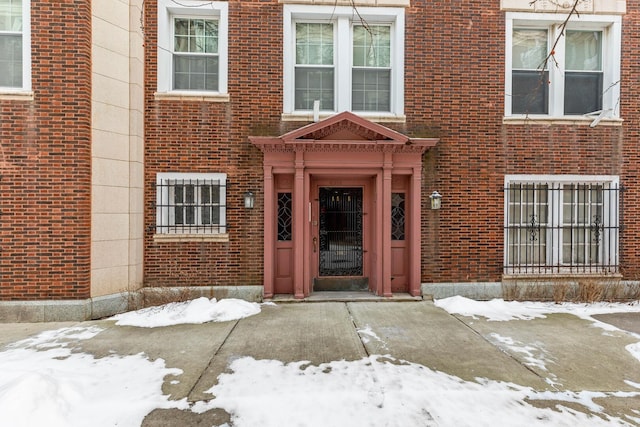 snow covered property entrance featuring brick siding