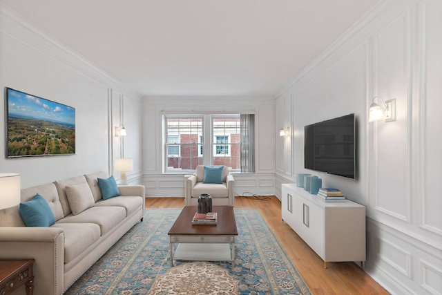 living room featuring crown molding, a decorative wall, and light wood-style flooring