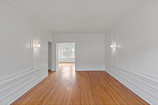 empty room with ornamental molding, light wood-type flooring, and a decorative wall