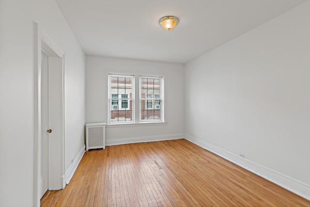 empty room with radiator heating unit, baseboards, and light wood-style flooring