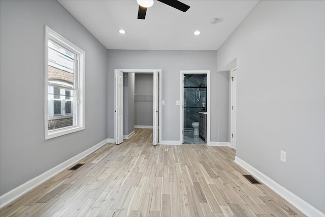 unfurnished bedroom with a closet, light hardwood / wood-style floors, ensuite bath, a walk in closet, and ceiling fan