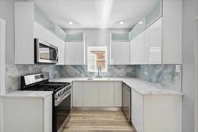 kitchen featuring light stone counters, sink, white cabinetry, appliances with stainless steel finishes, and light wood-type flooring