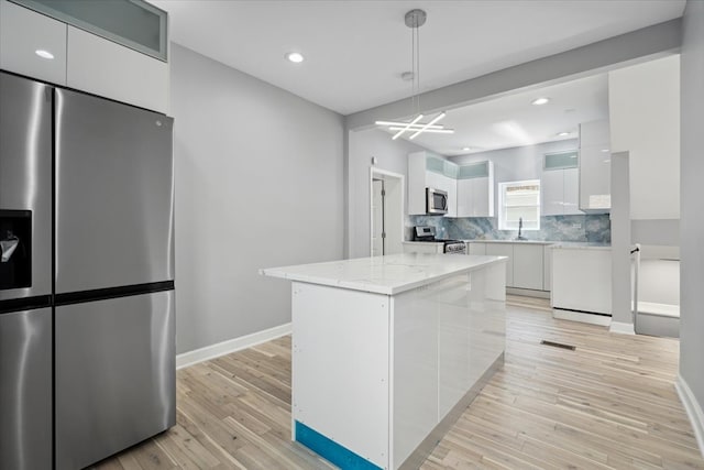 kitchen featuring light hardwood / wood-style floors, white cabinetry, pendant lighting, stainless steel appliances, and a center island