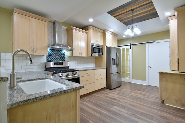 kitchen featuring light hardwood / wood-style flooring, a barn door, appliances with stainless steel finishes, wall chimney range hood, and a tray ceiling