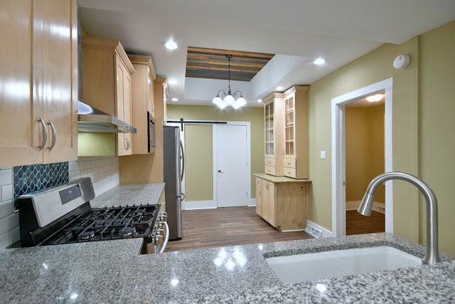 kitchen featuring wall chimney exhaust hood, appliances with stainless steel finishes, hanging light fixtures, a barn door, and light wood-type flooring