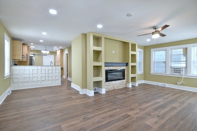 unfurnished living room with dark hardwood / wood-style floors, plenty of natural light, ceiling fan, and a stone fireplace