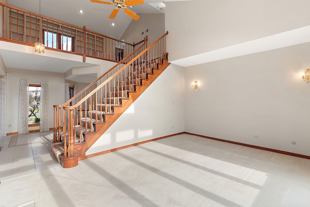 staircase with ceiling fan, carpet floors, and high vaulted ceiling