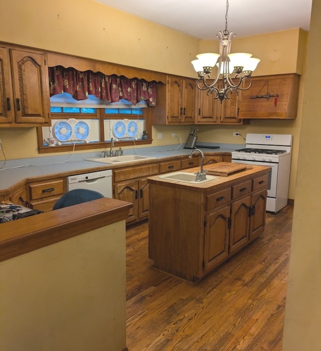 kitchen featuring white appliances, dark hardwood / wood-style flooring, pendant lighting, a kitchen island with sink, and a chandelier