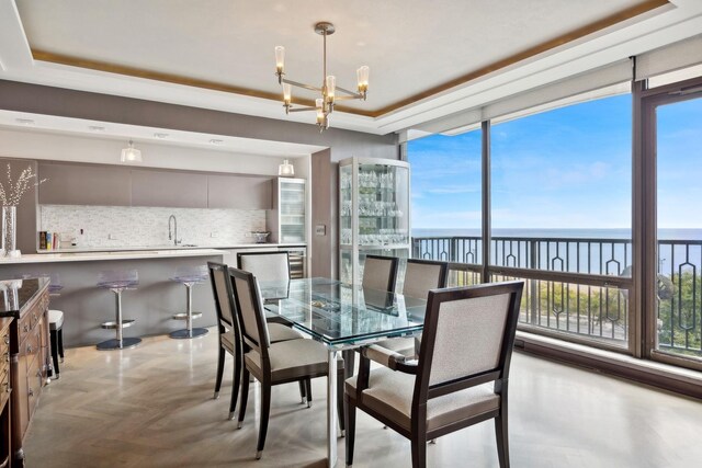 dining room featuring a notable chandelier, a raised ceiling, a water view, and plenty of natural light