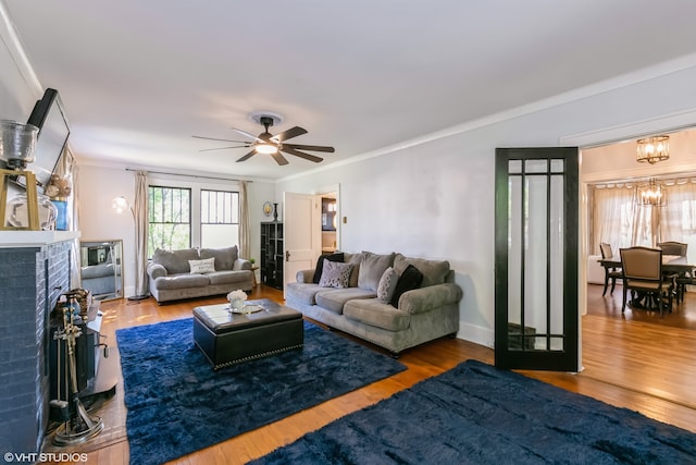 living room featuring wood-type flooring, ceiling fan with notable chandelier, a fireplace, and ornamental molding