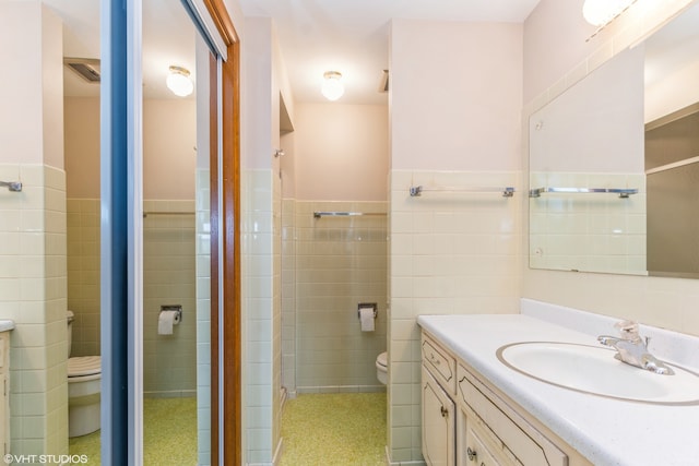 bathroom with tile walls, a shower with shower door, vanity, and toilet