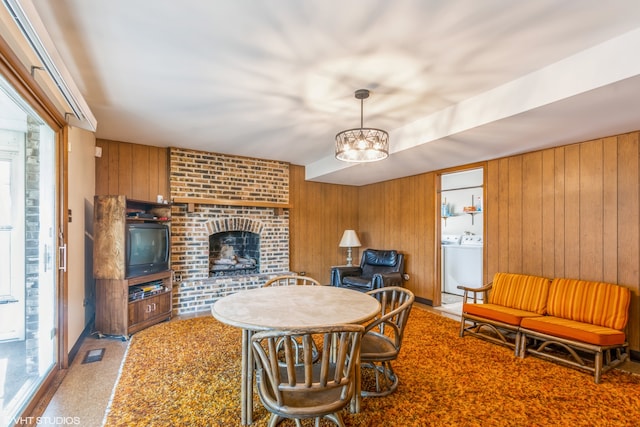 dining room featuring a chandelier, a fireplace, carpet flooring, wooden walls, and washer and dryer