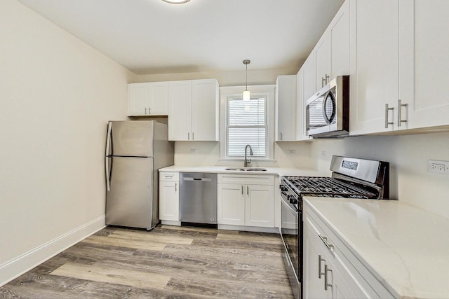 kitchen featuring pendant lighting, sink, white cabinetry, light hardwood / wood-style flooring, and appliances with stainless steel finishes