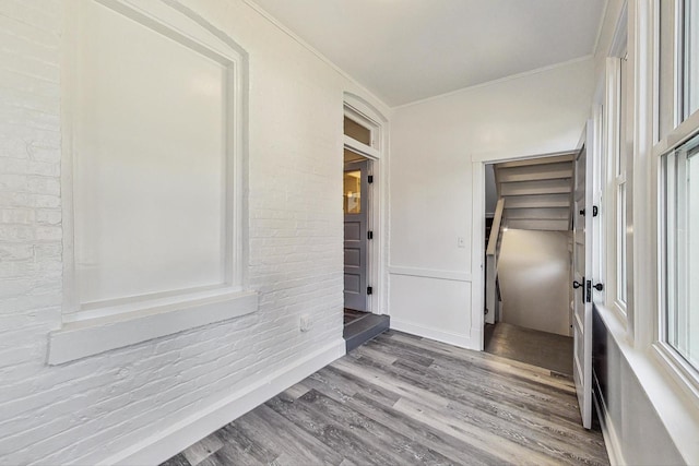 interior space featuring wood-type flooring, a wealth of natural light, brick wall, and crown molding