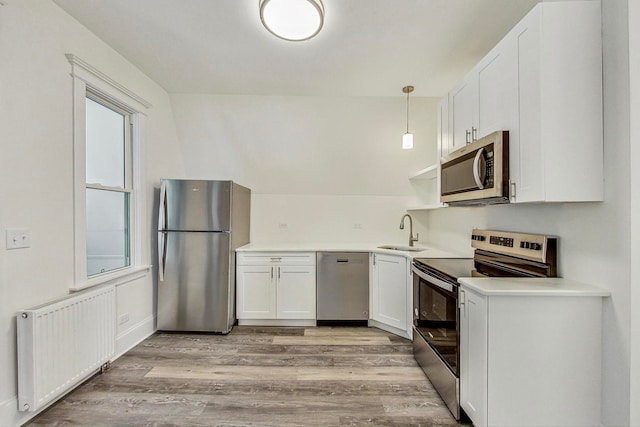 kitchen featuring white cabinetry, hanging light fixtures, light hardwood / wood-style flooring, appliances with stainless steel finishes, and radiator heating unit