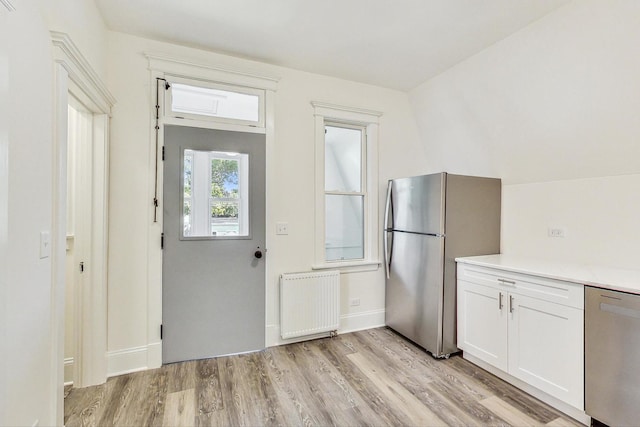 kitchen featuring radiator, appliances with stainless steel finishes, white cabinets, and light hardwood / wood-style flooring