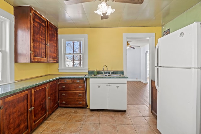 kitchen featuring arched walkways, a ceiling fan, dark countertops, freestanding refrigerator, and a sink