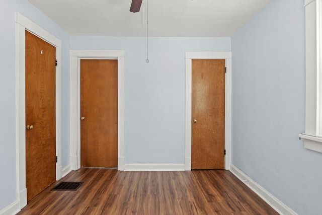 empty room featuring ceiling fan, dark wood finished floors, visible vents, and baseboards