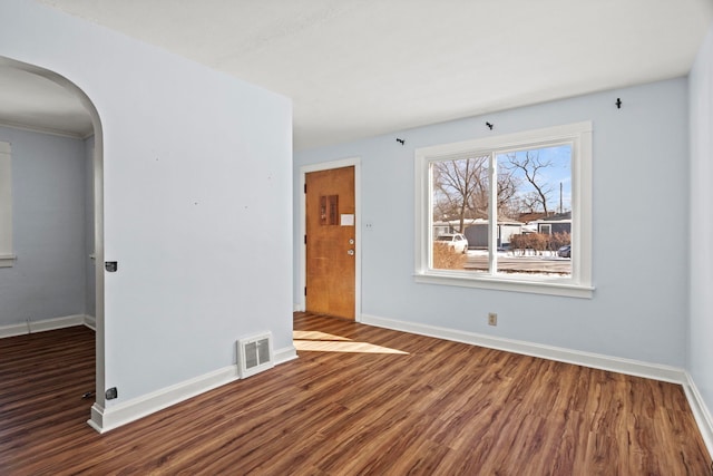 spare room with dark wood-type flooring, arched walkways, visible vents, and baseboards