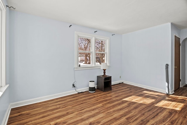 unfurnished room featuring arched walkways, dark wood finished floors, and baseboards