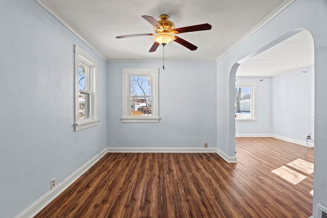 spare room featuring dark wood-type flooring, arched walkways, ornamental molding, and baseboards