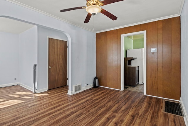 empty room featuring arched walkways, dark wood-type flooring, and visible vents