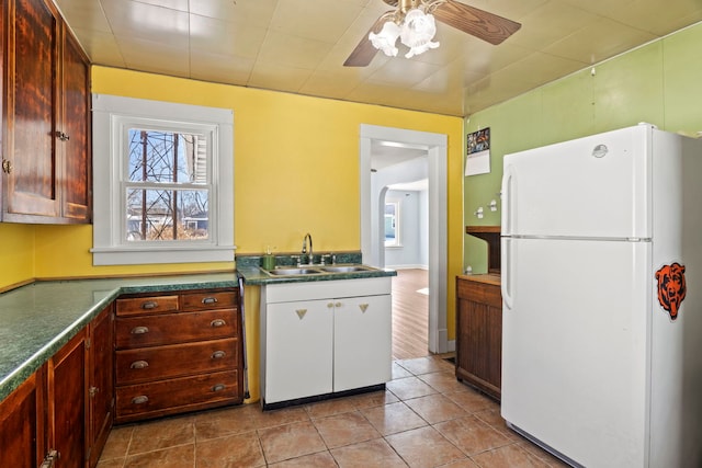 kitchen with light tile patterned flooring, a sink, a ceiling fan, freestanding refrigerator, and dark countertops