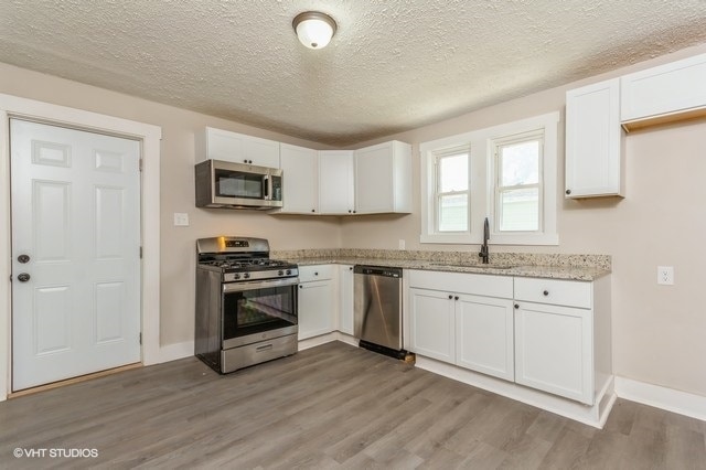 kitchen featuring wood-type flooring, white cabinets, appliances with stainless steel finishes, and sink