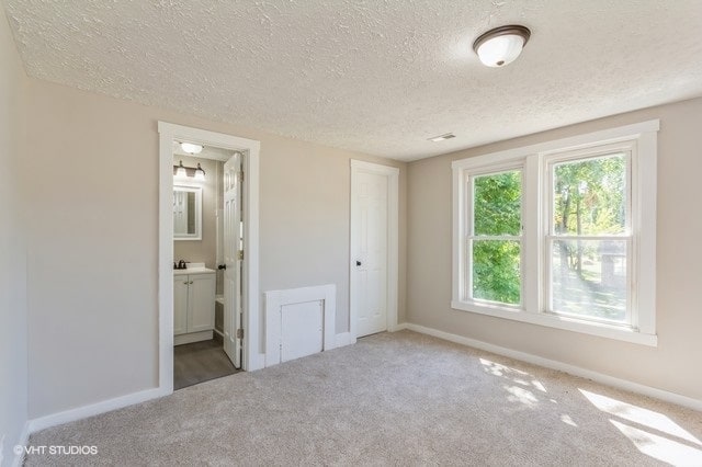 unfurnished bedroom featuring a textured ceiling, ensuite bath, and carpet flooring