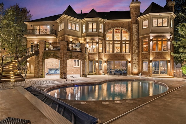 back house at dusk featuring a balcony and a patio area