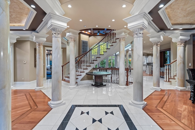 entryway with decorative columns, tile patterned floors, ornamental molding, and a raised ceiling