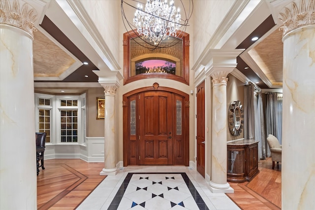 entryway featuring ornate columns, a chandelier, ornamental molding, a raised ceiling, and a high ceiling