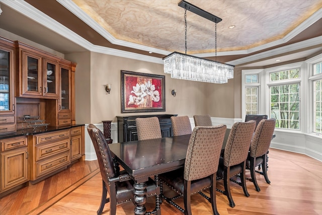 dining area featuring ornamental molding, light wood-type flooring, a notable chandelier, and a tray ceiling