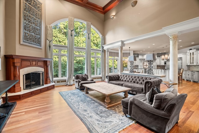 living room with light hardwood / wood-style floors, a high ceiling, crown molding, and decorative columns