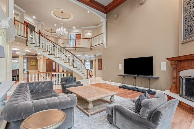 living room featuring a towering ceiling, a notable chandelier, decorative columns, crown molding, and light hardwood / wood-style flooring