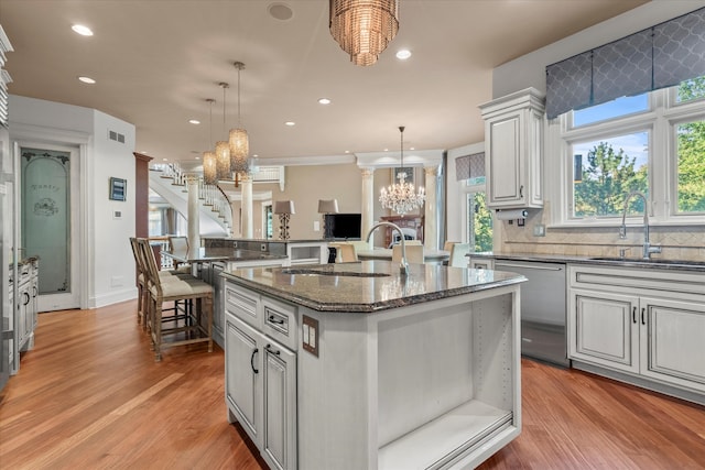 kitchen with sink, stainless steel dishwasher, a kitchen island with sink, light hardwood / wood-style flooring, and pendant lighting