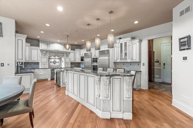 kitchen featuring tasteful backsplash, a center island, built in appliances, pendant lighting, and light hardwood / wood-style flooring