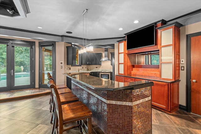 kitchen featuring dark stone countertops, decorative light fixtures, stainless steel electric range, a kitchen island, and wall chimney range hood