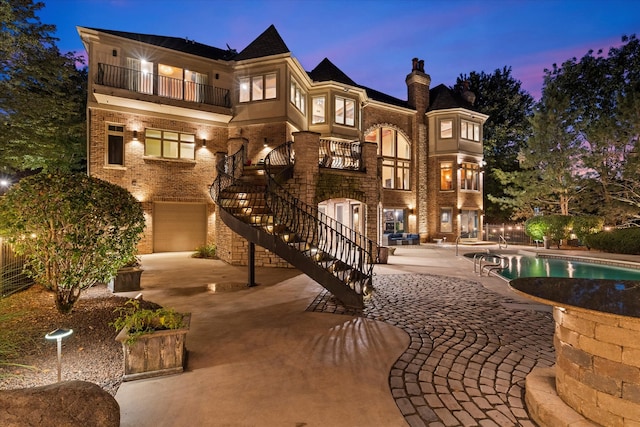 back house at dusk featuring a garage and a balcony