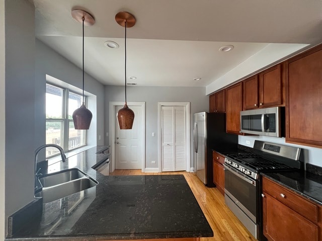 kitchen featuring light hardwood / wood-style floors, sink, stainless steel appliances, decorative light fixtures, and dark stone countertops