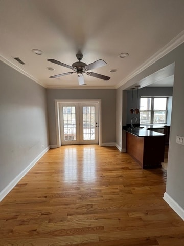 unfurnished living room featuring light hardwood / wood-style floors, ornamental molding, ceiling fan, and french doors