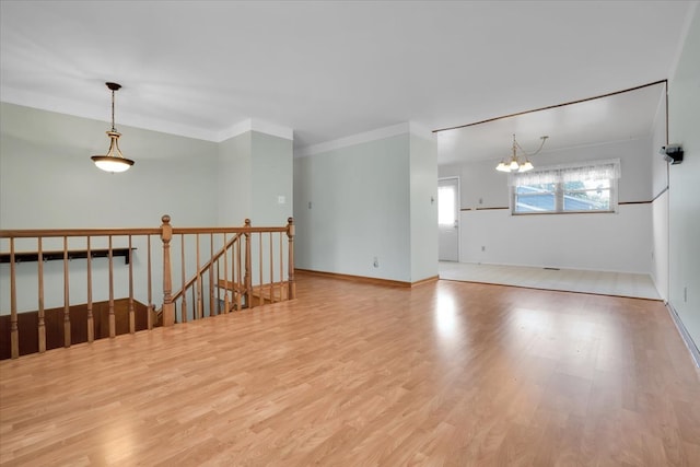 empty room with an inviting chandelier, light wood-type flooring, and crown molding