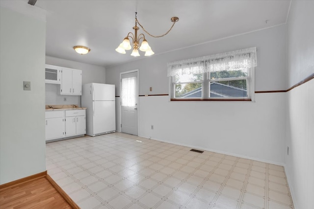 interior space with a wall unit AC, white cabinets, hanging light fixtures, white fridge, and an inviting chandelier