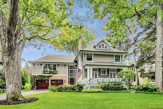 view of front of home with a porch, driveway, a chimney, a front yard, and an attached garage