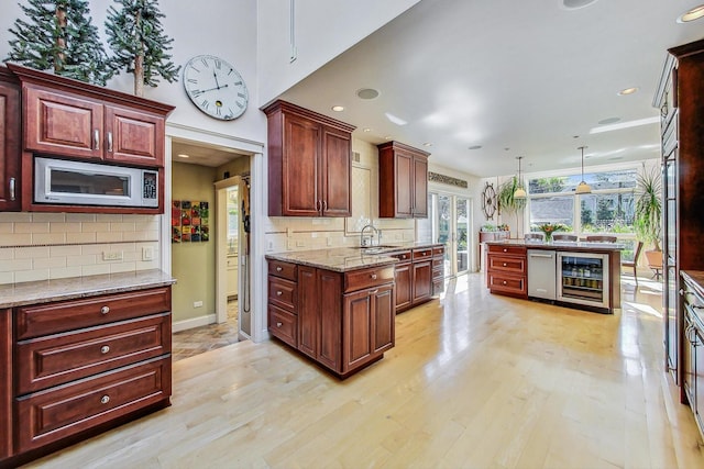 kitchen featuring a sink, light wood-style floors, stainless steel microwave, tasteful backsplash, and wine cooler