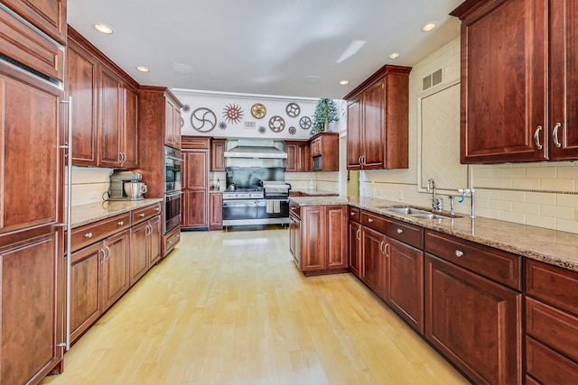 kitchen featuring wall chimney exhaust hood, a sink, light wood finished floors, backsplash, and premium appliances