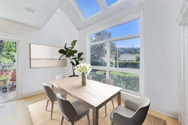 dining space featuring baseboards, light wood-type flooring, lofted ceiling with skylight, and visible vents