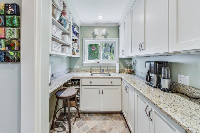 kitchen featuring a sink, white cabinets, light stone countertops, and crown molding