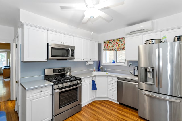 kitchen with white cabinets, a wall mounted AC, ceiling fan, appliances with stainless steel finishes, and light wood-type flooring